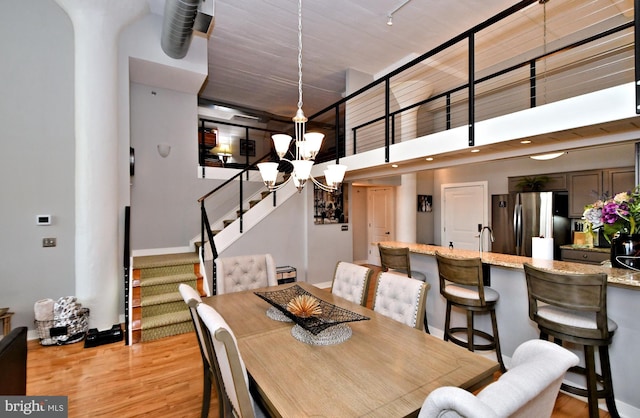 dining area featuring a towering ceiling, light wood finished floors, stairs, and a notable chandelier