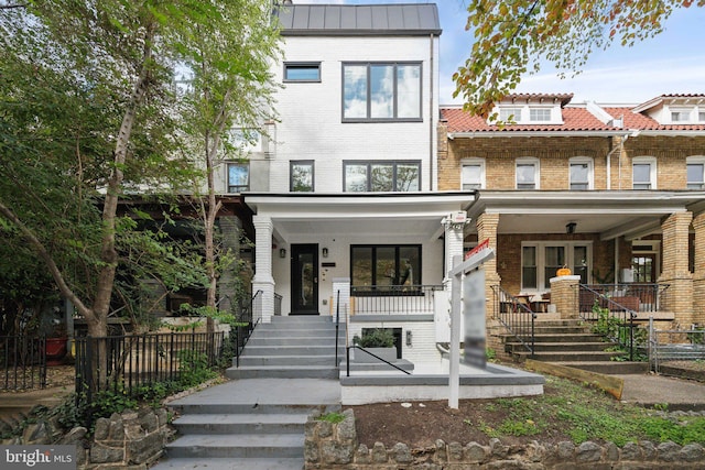 view of front of house with a porch, metal roof, brick siding, and fence