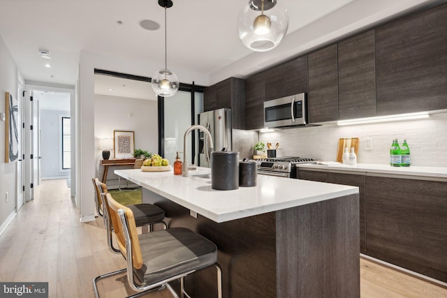 kitchen with light wood-style flooring, appliances with stainless steel finishes, light countertops, and backsplash