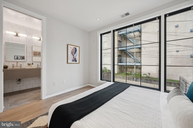 bedroom featuring baseboards, visible vents, wood finished floors, ensuite bathroom, and access to outside