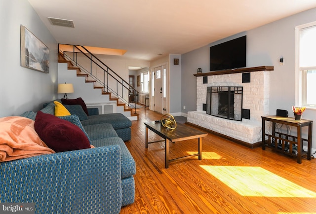 living room featuring visible vents, a fireplace with raised hearth, stairway, wood finished floors, and a healthy amount of sunlight