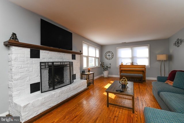 living area with a fireplace with raised hearth, hardwood / wood-style flooring, and baseboards