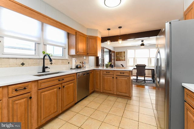 kitchen featuring brown cabinets, backsplash, appliances with stainless steel finishes, a sink, and a peninsula