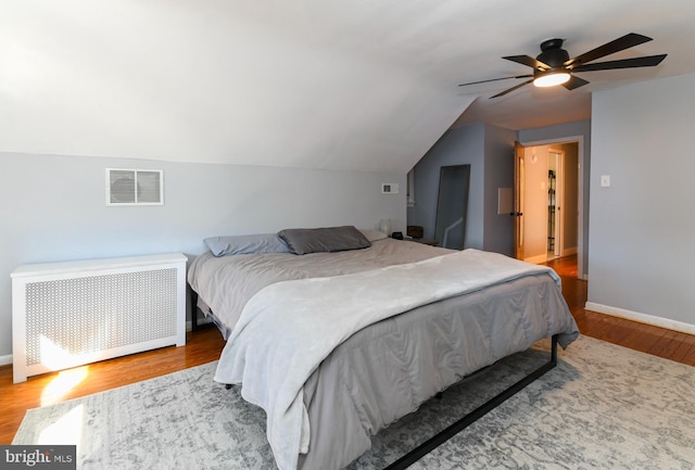 bedroom featuring wood finished floors, visible vents, baseboards, vaulted ceiling, and radiator heating unit