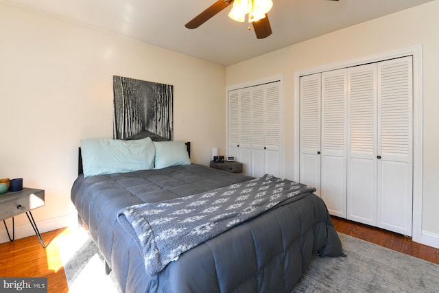 bedroom featuring a ceiling fan, baseboards, multiple closets, and wood finished floors