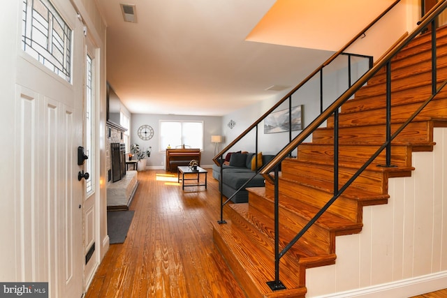 foyer entrance featuring baseboards, visible vents, a fireplace with raised hearth, hardwood / wood-style flooring, and stairs