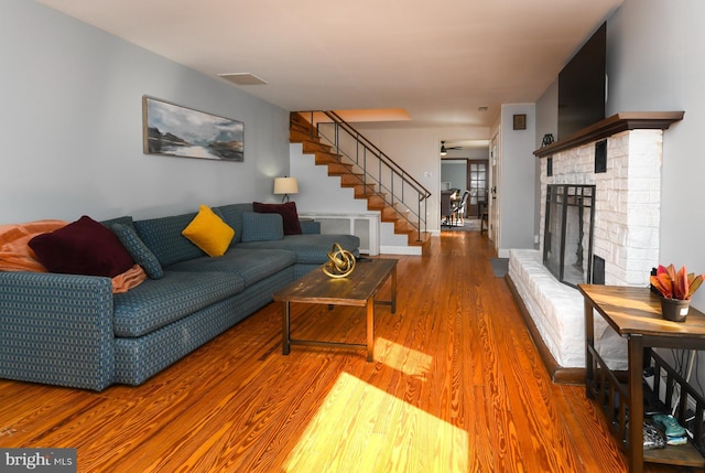 living room with visible vents, radiator heating unit, wood finished floors, stairs, and a brick fireplace