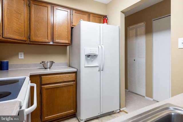 kitchen with built in desk, brown cabinets, white appliances, and light countertops