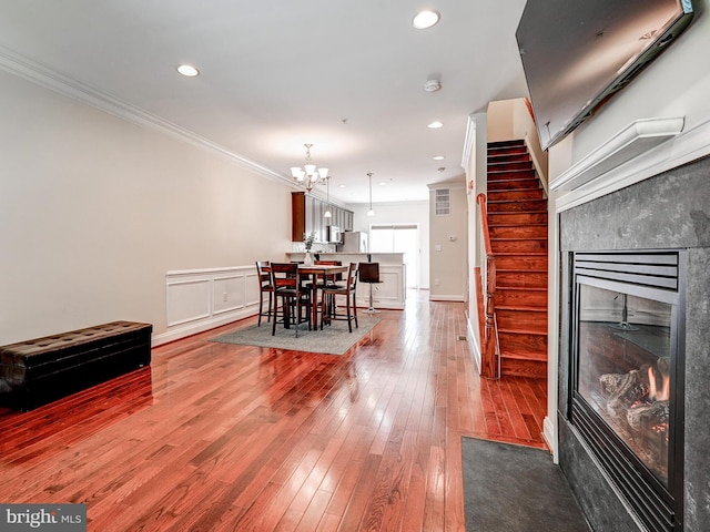 dining room with hardwood / wood-style flooring, recessed lighting, stairs, ornamental molding, and a glass covered fireplace