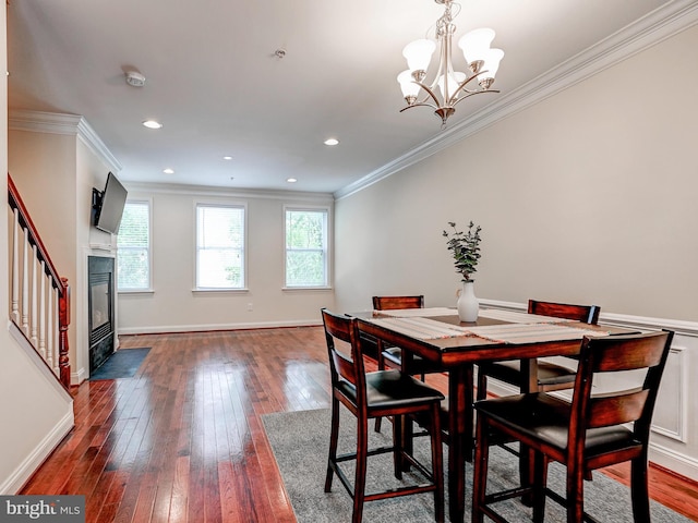 dining room with a fireplace with flush hearth, wood-type flooring, ornamental molding, and baseboards