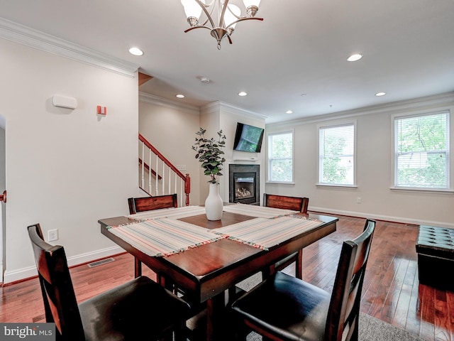 dining area with ornamental molding, hardwood / wood-style floors, a glass covered fireplace, and visible vents