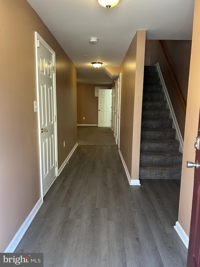 corridor with dark wood-type flooring, stairway, and baseboards