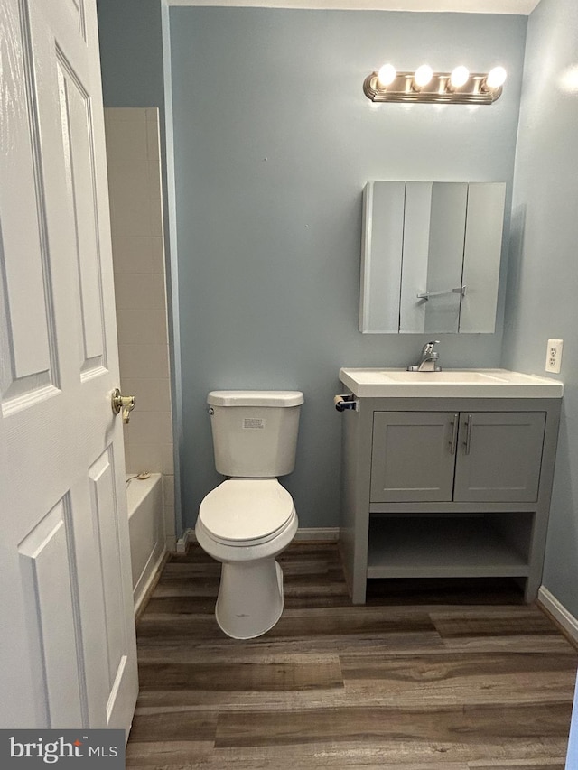 bathroom featuring toilet, washtub / shower combination, vanity, wood finished floors, and baseboards