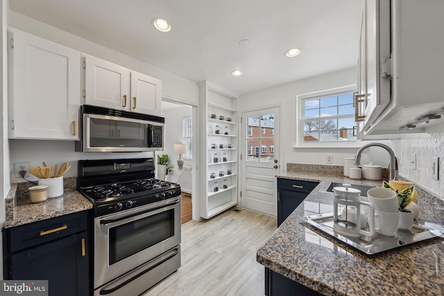 kitchen with recessed lighting, stainless steel appliances, a sink, white cabinetry, and dark stone countertops