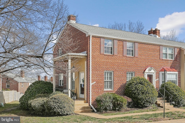 view of front of property featuring brick siding, a chimney, a shingled roof, and fence