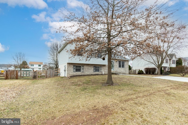 split level home featuring a front lawn, fence, and brick siding