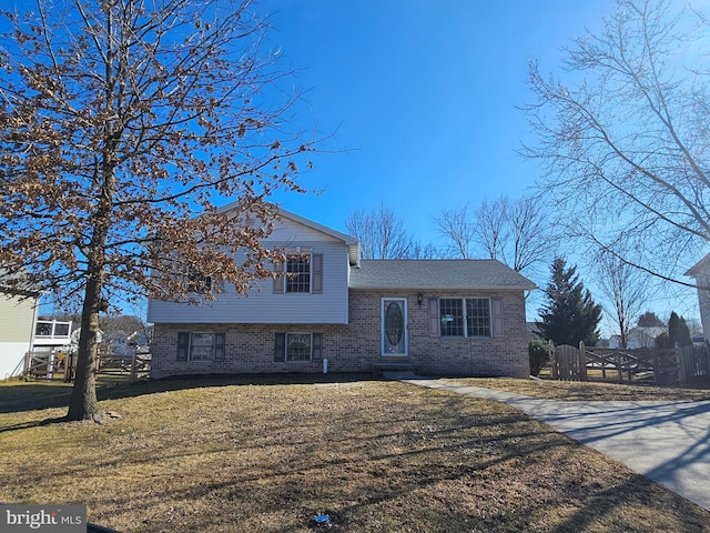 split level home with brick siding, a front lawn, and fence