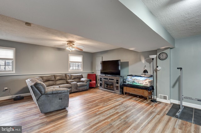 living area with a textured ceiling, ceiling fan, wood finished floors, visible vents, and baseboards