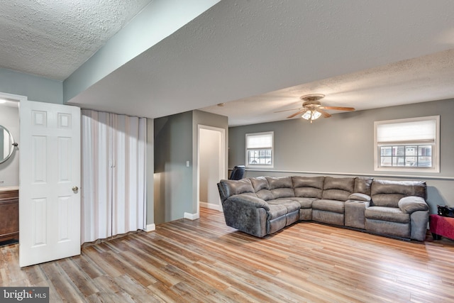 living area with baseboards, ceiling fan, a textured ceiling, and light wood finished floors