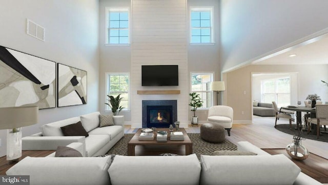 living room featuring a large fireplace, visible vents, baseboards, and wood finished floors