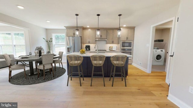 kitchen with pendant lighting, washer / clothes dryer, light countertops, appliances with stainless steel finishes, and light wood-type flooring