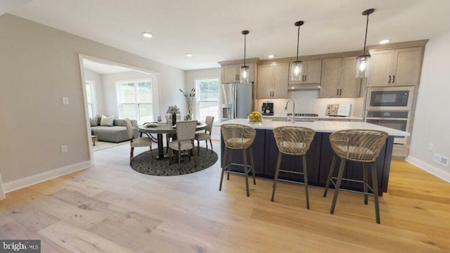 kitchen featuring a center island with sink, decorative light fixtures, stainless steel appliances, light countertops, and backsplash