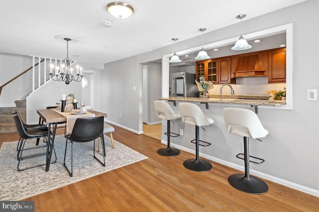 dining area featuring light wood-style floors, stairs, baseboards, and a notable chandelier