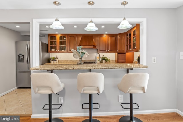 kitchen featuring decorative backsplash, brown cabinets, stainless steel refrigerator with ice dispenser, and a kitchen bar