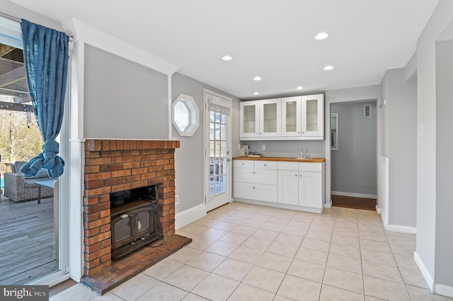 kitchen featuring light tile patterned floors, a sink, baseboards, white cabinets, and glass insert cabinets