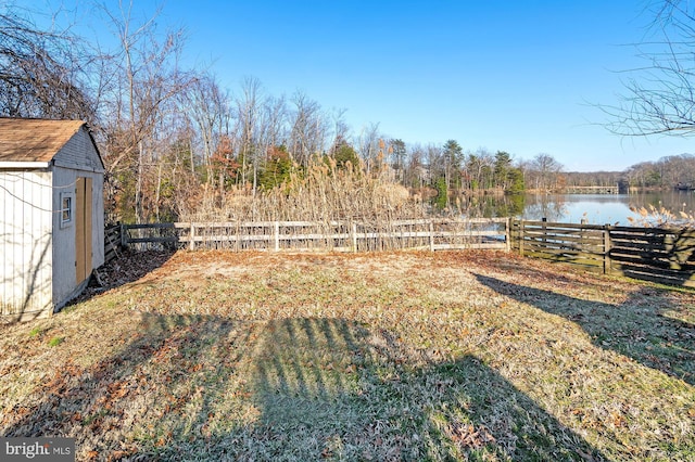 view of yard featuring a water view, fence private yard, a storage shed, and an outdoor structure