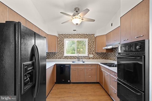 kitchen featuring light wood-style flooring, backsplash, a sink, under cabinet range hood, and black appliances