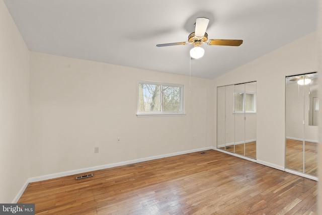 unfurnished bedroom with multiple closets, lofted ceiling, light wood-style floors, and baseboards