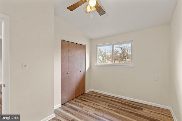 unfurnished bedroom with light wood finished floors, a closet, a ceiling fan, vaulted ceiling, and baseboards