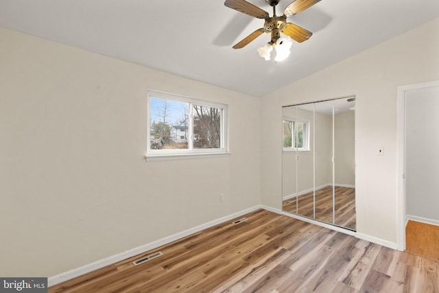 unfurnished bedroom featuring baseboards, visible vents, light wood-style flooring, vaulted ceiling, and a closet