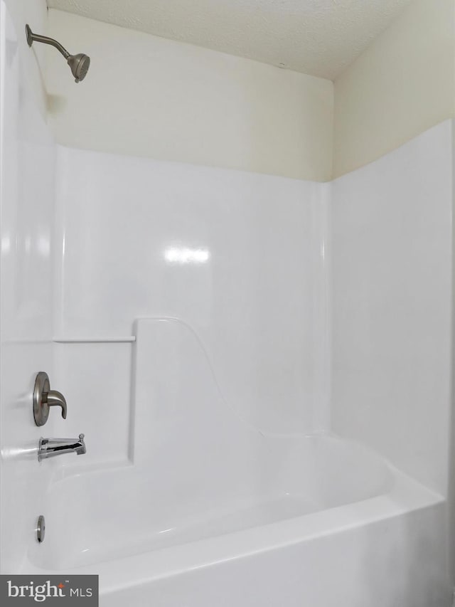 bathroom with a textured ceiling and bathtub / shower combination