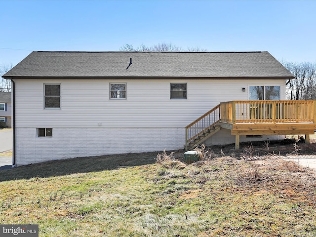 rear view of house featuring brick siding, a shingled roof, a deck, and a yard