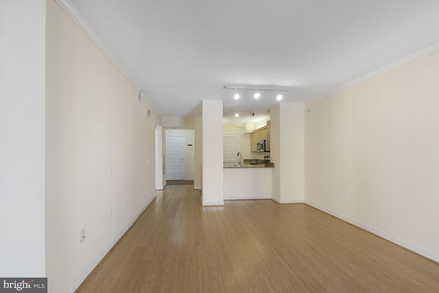 unfurnished living room with light wood-type flooring, a sink, crown molding, and baseboards