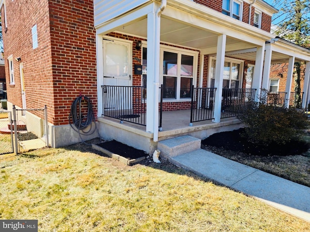 entrance to property with covered porch, fence, and brick siding