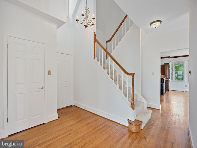 foyer entrance featuring stairway, an inviting chandelier, baseboards, and wood finished floors