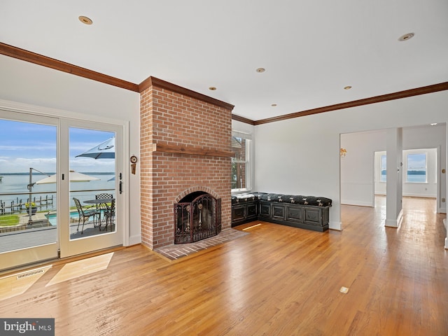 unfurnished living room featuring a healthy amount of sunlight, visible vents, ornamental molding, a brick fireplace, and light wood-type flooring