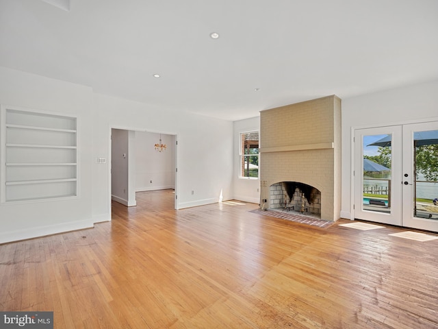 unfurnished living room with built in features, french doors, a fireplace, light wood finished floors, and baseboards