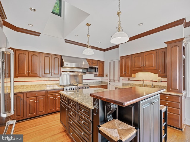 kitchen featuring an island with sink, ornamental molding, stainless steel microwave, wall chimney range hood, and light wood-type flooring