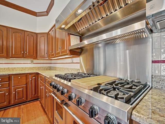 kitchen with crown molding, premium range hood, cooktop, light stone counters, and brown cabinetry