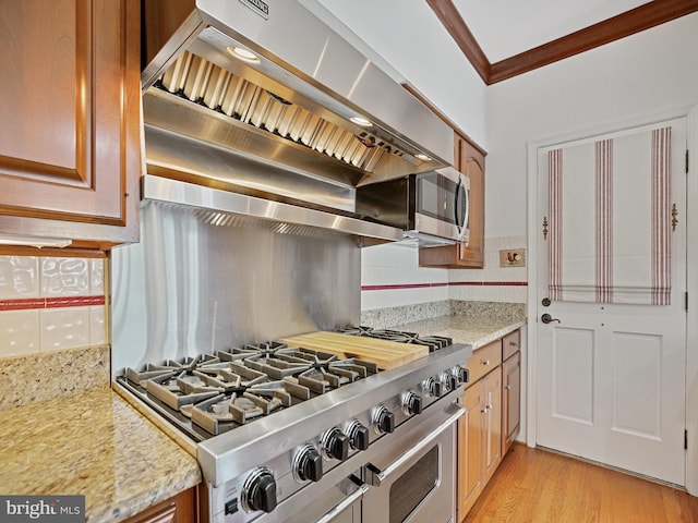 kitchen with light stone counters, range with two ovens, ornamental molding, light wood-type flooring, and backsplash