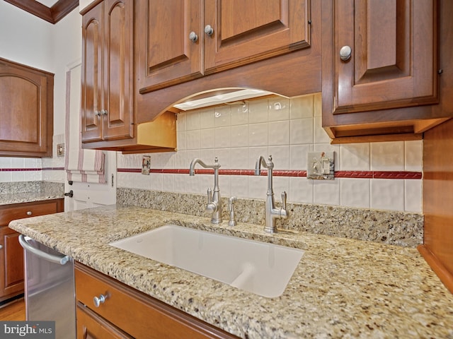 kitchen featuring light stone countertops, brown cabinetry, backsplash, and a sink