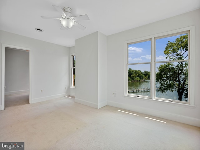 empty room featuring visible vents, light colored carpet, a ceiling fan, and baseboards