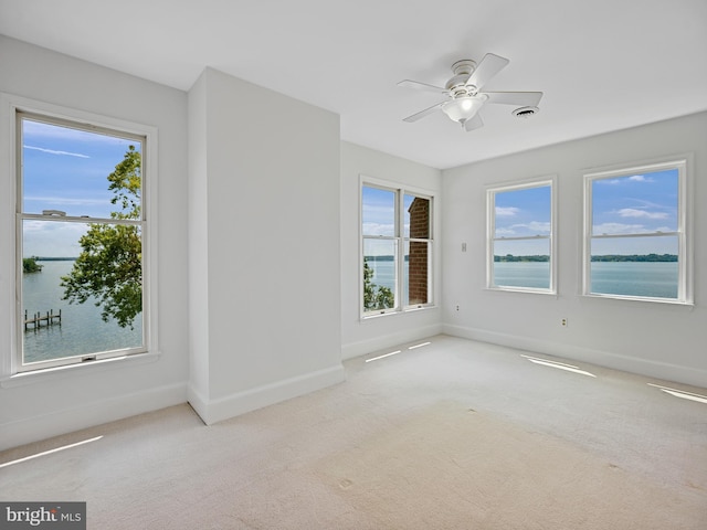 carpeted empty room with visible vents, ceiling fan, baseboards, and a water view