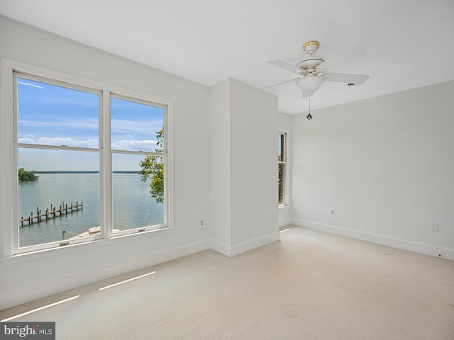 spare room with light colored carpet, ceiling fan, baseboards, and a water view