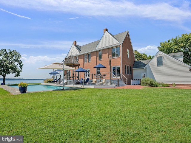 rear view of house with a lawn, an outdoor pool, and a water view