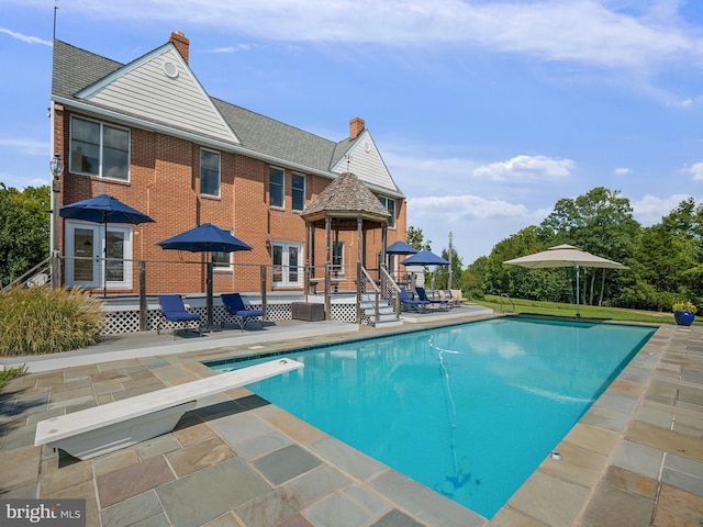 outdoor pool with french doors, a patio, and a diving board